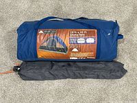 Photo of folded Ozark Trail dome tent in blue carrying bag with attached label showing tent image and specifications.
