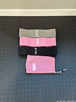 Three fabric resistance bands arranged stacked by resistance level with a pink mesh pouch at bottom