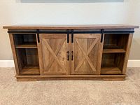 Front view of rustic wood TV stand with closed sliding barn doors and side shelves visible.