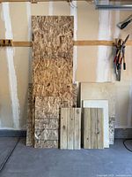 Front view of scrap OSB, plywood and miscellaneous wood boards leaning against garage wall, showing variety of sizes and wood textures.