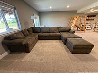 Full view of U-shaped green suede sectional couch arranged with ottoman in a carpeted living space, showing sectional design and plush cushions.