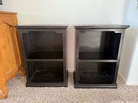 Front view of both black wooden nightstands side by side showing shelves and top surfaces.