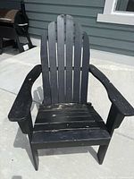 Front view of one black wooden Adirondack chair showing slatted seat and weathering on paint.
