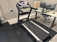 Full side view of Sole F80 treadmill showing running belt and folding frame on black floor mat under office desk.