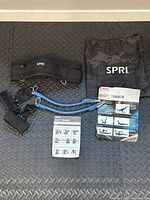 All lot contents arranged including adjustable belt, resistance tubes, mesh bag with SPRI logo, and instruction manuals on a black textured surface