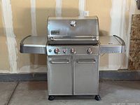 Front view of stainless steel Weber Genesis grill with side shelves and two-door cabinet on casters