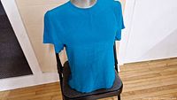 Front view of a bright blue silk blouse on a mannequin seated on a chair, showing crew neckline and short sleeves.