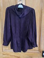 Back view of brown silk long-sleeve shirt showing the smooth fabric, gathered cuffs and hem, hanging on wood background.