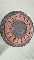 Top view of first round cast iron floor grate showing the decorative inner medallion and curved cut-out pattern with rust and dirt.