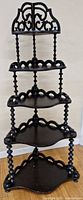 Full view of the antique black wooden corner shelf showing four tiers with spool supports and decorative top.