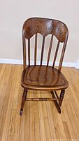 Front view of the antique wooden rocking chair showing perforated backrest and seat, curved back with spindles, and rocker base.