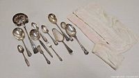 Full view of all assorted vintage silver-plated utensils arranged together with fabric pouch