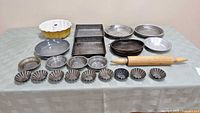 Full view of bakeware showing all items including wooden rolling pin, yellow bundt pan, rectangular baking pans, round cake and pie tins, and tart tins.