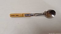 Metal musical spoon with wooden handle labeled 'Dorey Dan'