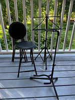 Photo of black adjustable music stand, guitar stand, and two collapsible stools on a porch.