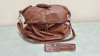 Front view of brown genuine leather shoulder bag with attached adjustable shoulder strap, displayed on a light surface.