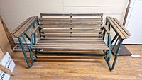 Front and side view of the glider garden bench showing its metal frame and wooden slats seat and backrest.