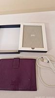 Kobo e-reader in box with purple leather case and USB cable laid out on a white surface.