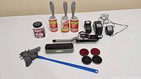Photo showing all items together on a white surface: 3 lint rollers, fabric powder, rectangular brush, electronic fly swatter, circular brushes, and battery chargers.