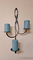 Full view of black metal wall-mounted candle holder with three blue pillar candles attached.
