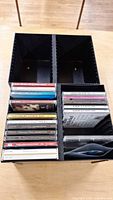 Overview of a black plastic CD holder with 26 CDs arranged inside, showing spines of various artists and compilations.