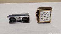 Opera glasses and travel clock side by side showing scale and condition.