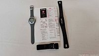 Polar fitness tracker watch, two black wrist straps, and user manual laid out on a white surface