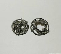 Front view of the two signed pewter brooches, showing the floral and leaf designs in polished pewter