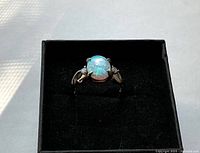 Close-up of the sterling silver ring with a multi-colored opal displaying blue and green flashes; ring presented inside a black jewelry box.