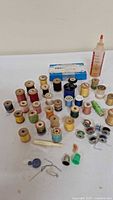Wide shot showing numerous wooden thread spools in varied colors, sewing machine oil bottle, and metal bobbins scattered on surface.