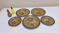 Five vintage ceramic plates arranged with floral motifs and two small glass bottles in yellow and amber color.