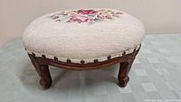 Full view of the foot stool showing round needlepoint floral cushion and wooden carved legs