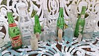 Full collection of vintage glass bottles shown on white ornate metal table outdoors