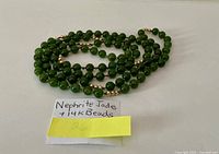 Coiled necklace on white background with note card reading 'Nephrite Jade + 14K Beads'