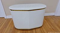 Photo of white oval laundry hamper with gold trim, showing front closed view