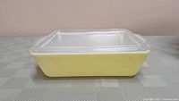 Side view of yellow Pyrex keeper dish with ribbed clear glass lid showing yellow base and white interior walls