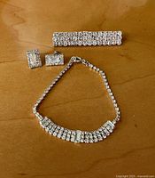 Top view of vintage rhinestone brooch, bracelet, and earrings on wooden surface.
