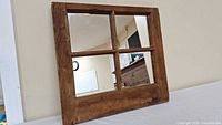 Square wall mirror with wooden frame divided into four panes, photo showing mirror reflecting room interior.