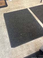 Close-up view of a large black rubber-backed floor mat showing texture and condition
