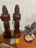 Pair of wooden male sculptures with shields and a ceramic bald eagle on a wooden base.