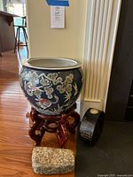 Ceramic planter with colorful birds and fish on wooden stand alongside elephant votive candle holders and rectangular rock doorstop on the floor.