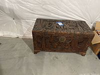 Photo of entire wood chest showing rectangular shape, dark stain, carved top and front panels, and feet.