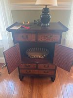 Full view of side table with drawers and double doors open displaying woven basket inside on shelf.