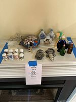 Various vanity top items including thimbles, perfume bottles, pottery containers, figurines, and decorative pieces arranged on a white mantle above a fireplace