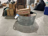Large galvanized aluminum bucket placed on concrete floor with other boxed items around.
