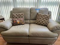 Front view of beige leather loveseat with two throw pillows