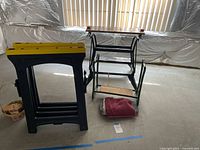 Black and Decker Workmate folding workbench with two plastic construction horses in background, towel and paper on floor.