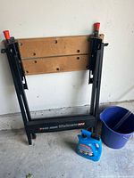 Folded Black & Decker Workmate 300 worktable leaning against a white wall, next to a blue bucket and a bottle of mildew stain remover.