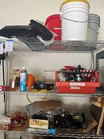 Wide view of shelf with red, white, and gray plastic buckets, black extension cords, car maintenance cleaning items like sprays and brushes, cleaning caddy labeled 'CLEAN CAR', and other maintenance tools and mats.