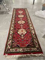 Full view of the red oriental carpet runner with decorative border and fringe ends laid out on gray floor.
